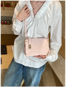 Detail of light pink leather crossbody bag with gold rivets and turn-lock on a model