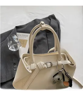 Detail of cream leather handbag with dual handles and stylish horse charm accessory