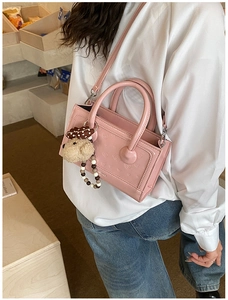 Detail of pink patent leather handbag featuring dog flower embossing and teddy bear charm