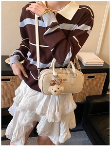 Détail du sac Boston crème avec breloque ours et bandoulière amovible sur mannequin