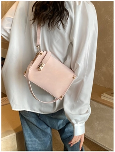 Pink crossbody bag with gold turn-lock buckle shown on shoulder for size reference