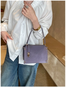 Detail of purple small shoulder bag with gold metal rivets and lock on blue denim