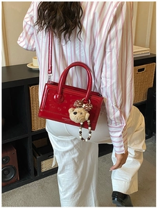 Detail of red embossed crossbody bag with plush bear charm worn with striped shirt
