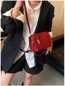 Detail of red crossbody bag with gold buckle hardware and metal rivets on black suit