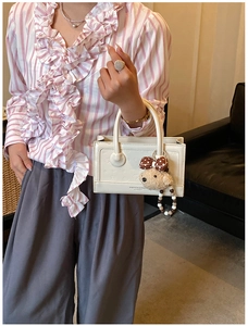 Detail of cream white handbag with embossed texture, fashion print and a cute bear charm