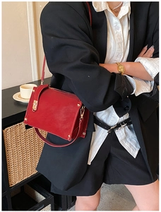 Close-up of red leather rectangular shoulder bag with metal twist lock on black suit outfit