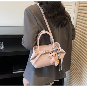 Detail of light pink leather handbag with decorative pony charm and shoulder strap on model