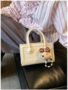 Detail of cream white leather handbag featuring puppy embossing and plush bear charm