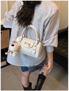 White cylinder bowling bag with gold hardware, detachable strap, and cute plush dog charm