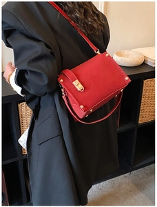 Detail of red suede shoulder bag with gold metal clasp and rivets on black blazer