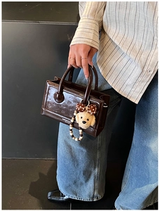 Detail of vintage brown patent leather handbag with embossed texture and teddy charm
