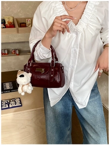 Detail of burgundy glossy leather bucket bag with cute white plush puppy charm and metal handle