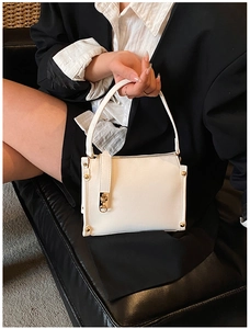 Close-up of a white leather handbag with gold studs held by a model in a black blazer