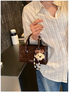 Detail of a brown patent leather handbag with a plush puppy charm and beaded chain