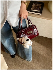 Detail of burgundy patent leather cylinder bag with plush puppy charm and metallic plate