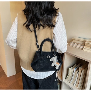 Detail of a matte black vintage tote bag with a small horse charm and long shoulder strap