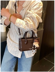 Brown patent leather handbag with bear charm shown in a lifestyle model setting