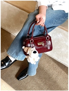 Detail of burgundy patent leather bowling bag with heart charm and teddy bear pendant