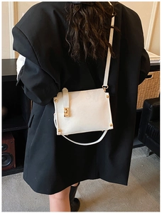 Close-up of white leather crossbody bag with gold twist lock and metal rivet details