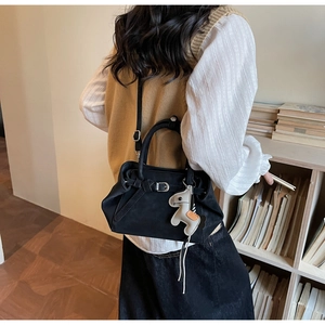 Detail of black suede tote bag with horse charm on shoulder of model in library
