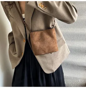 Petit sac seau en daim marron porté en bandoulière dans un décor intérieur minimaliste chic