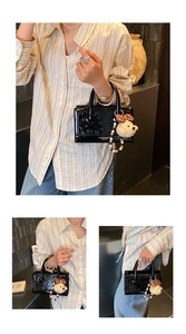 Detail of a black patent leather handbag featuring a plush bear charm and white lettering