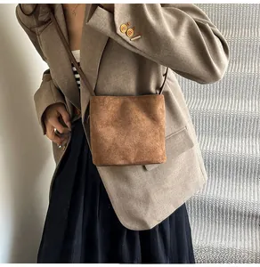 Gros plan sur un sac bandoulière en daim marron porté avec un blazer aux tons terre