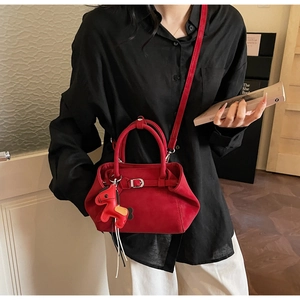 Detail view of red suede handbag with horse charm accessory and leather strap closure