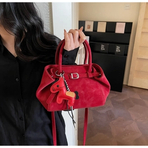 Detail of red suede handbag featuring a signature horse charm and metal buckle accent
