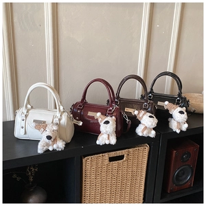 Detail of four stylish faux leather Boston bags with plush puppy charms on a wooden shelf