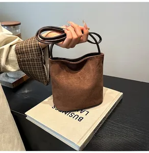 Détail d'un sac seau en daim marron café mat avec une poignée en cuir lisse