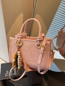 Pink textured crossbody bucket bag with wood bead charm and fashion logo print