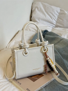 Elegant white square handbag with textured leather and decorative beaded tassel pendant