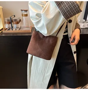 Gros plan détaillé du sac seau en daim marron avec fine bandoulière sur manteau beige