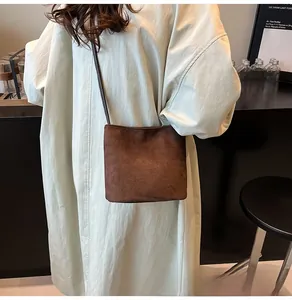 Détail du sac à bandoulière marron mat porté avec un manteau beige dans un cadre de café