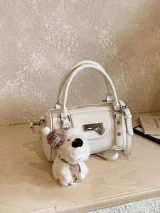 Cream-colored cylinder bowling bag with plush puppy charm and detachable strap