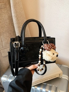 Glossy black leather handbag with embossed dog pattern and plush charm pendant