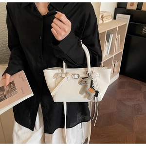 Detail of a beige leather handbag with belt buckle design and a horse charm accessory
