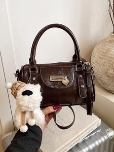 Dark brown glossy Boston bag with plush dog charm shown in a lifestyle travel setting