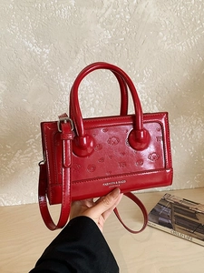 Glossy red handbag with embossed cartoon dog and bow pattern plus adjustable shoulder strap