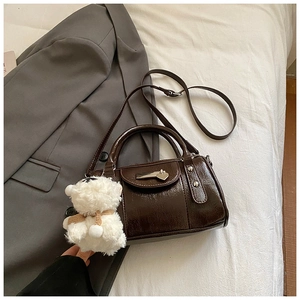 Detail der dunkelbraunen Lackleder-Boston-Tasche mit weißem Plüschbär-Anhänger als Zubehör