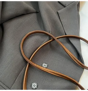 Détail de la bandoulière en cuir marron avec couture fine et bouton sur blazer gris