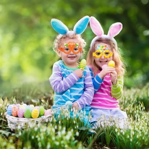 Kinder mit Osterbrillen aus Papier mit Hasen- und Herzmotiven auf einer grünen Wiese