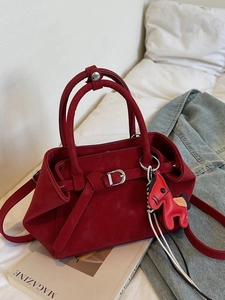 Minimalist red suede Boston handbag with buckle detail and horse charm in a cozy home setting