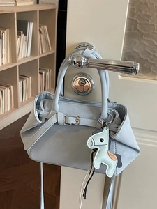 Minimalist light blue handbag with horse charm hanging on a door handle in a room