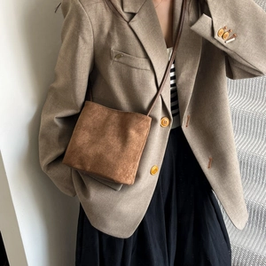 Petit sac bandoulière en daim marron porté par un mannequin dans un cadre chic