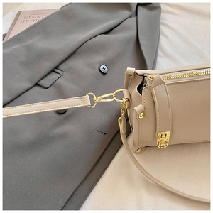 Detail of gold-tone metal hardware and stitching on a beige leather crossbody bag