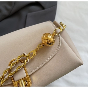 Close-up of beige crossbody bag featuring a golden ball chain and textured leather