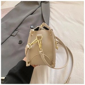 Detail of beige leather bag side with gold hook hardware and adjustable shoulder strap