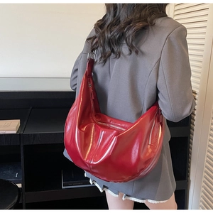 Détail d'un grand sac demi-lune rouge porté à l'épaule montrant le cuir brillant